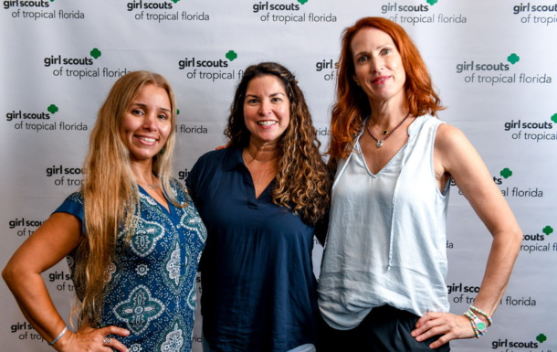 three girl scout volunteers posing in front of a girl scout step and repeat at a training in Miami, FL