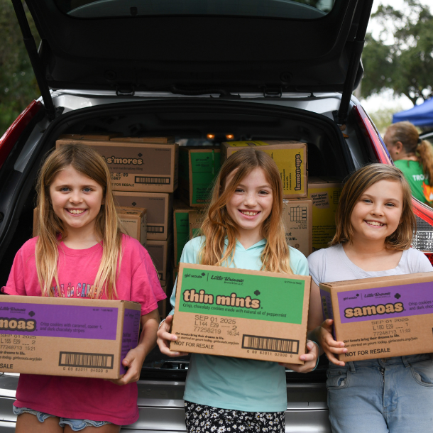 Three older Girl Scouts holding up a vest plus UM posters in the University of Miami U at Cookie U