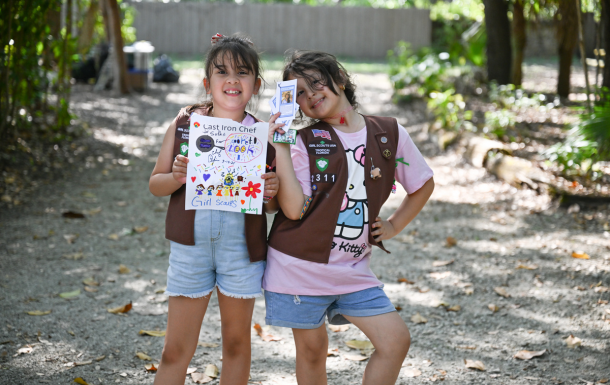 Girl Scout in tan vest holding up big box of samoas