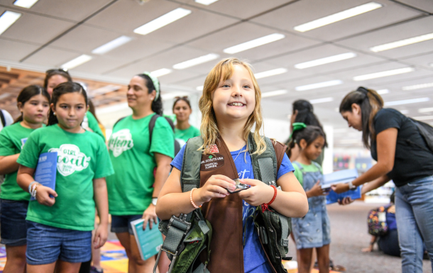 Brownie girl scout at GIRL Fest, smiling, with her friends behind her.
