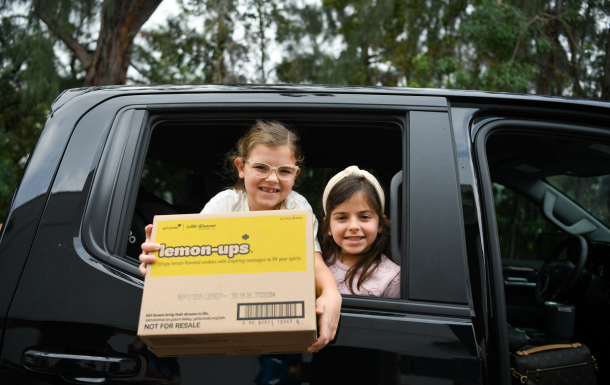 two girl scout brownies in vests holding up a handmade drawing of Cast Iron Chef event