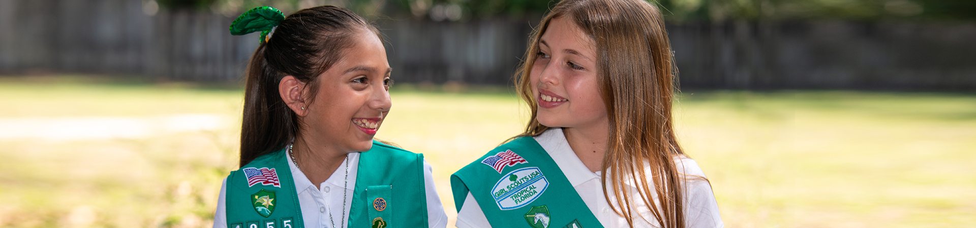  group of junior girl scouts walking outside hugging smiling at camera in junior vest and sash with badges 