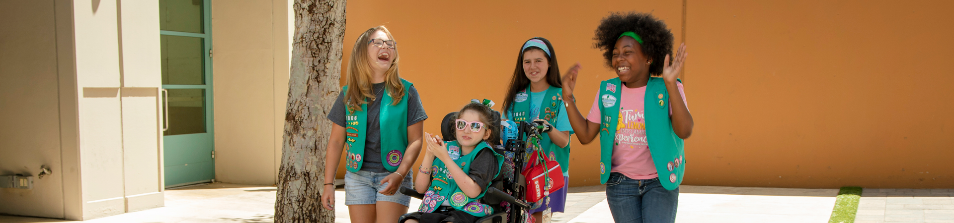  two girl scouts wearing trefoil clothing leaning on one another indoors 