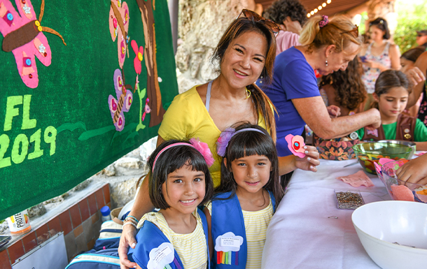 group of daisy girl scouts holding hands in uniform blue apron vest with patches and badges