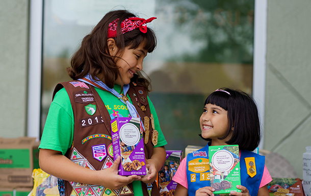 two adult volunteers with a group of girl scout daisies outside selling cookies
