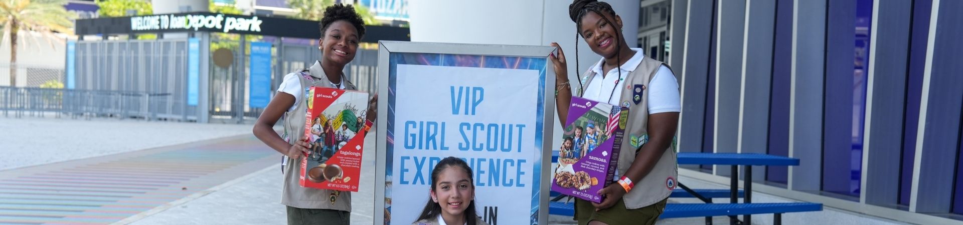  hands of young girl scout holding cookie box and handing it to a customer at an outdoor cookie booth 